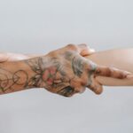 Due mani si stringono: una è completamente tatuata, l'altra no